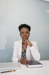 Selbstbewusste junge Geschäftsfrau mit Tagebuch am Schreibtisch sitzend im Büro - DCRF01491