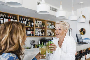 Glückliche Geschäftsfrau und Freundin stoßen mit Cocktails an der Bar im Restaurant an - DCRF01555