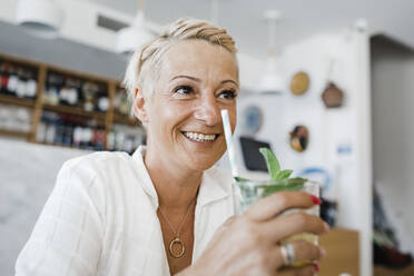 Happy blond woman with cocktail sitting in restaurant - DCRF01564