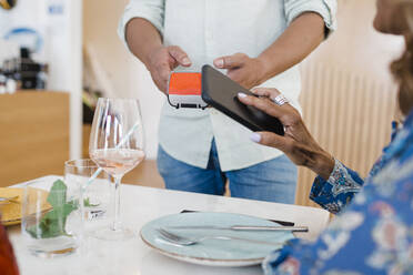 Mature businesswoman making payment through smart phone at restaurant - DCRF01566