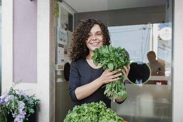 Happy entrepreneur with fresh leafy vegetables standing in front of door - DCRF01568