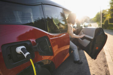 Electric car charging at station with woman disembarking from vehicle on sunny day - EKGF00153