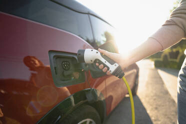 Hand of woman plugging charger in electric car at vehicle charging station - EKGF00156