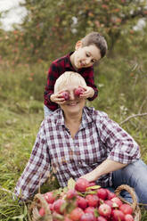Playful boy holding apples over grandmothers eyes at farm - ONAF00147