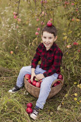 Verspielter Junge mit Apfel auf dem Kopf auf dem Bauernhof sitzend - ONAF00153