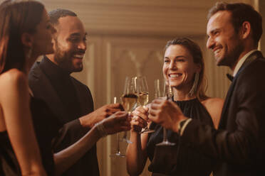 Eine Gruppe von Menschen bei einer Feier, die Wein trinken. Männer und Frauen in formeller Kleidung stoßen an und trinken Champagner auf einer Party. - JLPPF00027