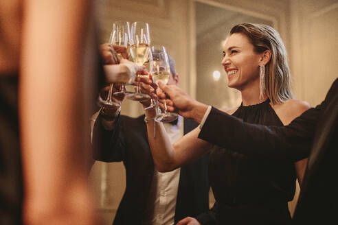 Eine multiethnische Gruppe von Menschen stößt mit Champagner an. Männer und Frauen stoßen mit Getränken auf einer Party an. - JLPPF00029
