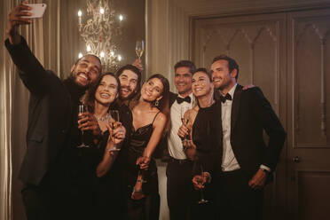 Ein Mann macht ein Selfie mit seinen Freunden auf einer Party. Eine Gruppe von Männern und Frauen stößt an und posiert für ein Selfie auf einer Feier. - JLPPF00037