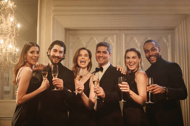 Eine Gruppe von Freunden feiert gemeinsam Silvester. Lächelnde multiethnische Männer und Frauen stehen zusammen, stoßen mit Champagner an und schauen in die Kamera. - JLPPF00050