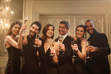 Eine Gruppe von Männern und Frauen feiert Silvester zusammen mit Champagner. Lächelnde multiethnische Freunde stoßen zusammen mit Champagner an und schauen in die Kamera. - JLPPF00051