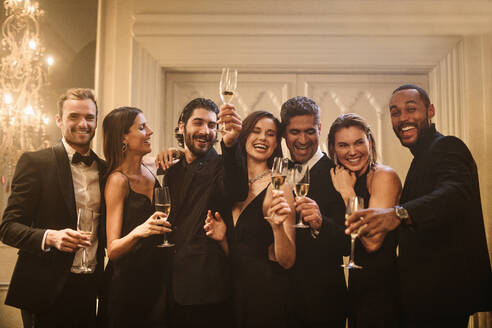 Eine bunt gemischte Gruppe von Menschen feiert mit Champagner auf einer Party. Multi-ethnische Freunde stoßen gemeinsam an und schauen in die Kamera. - JLPPF00052
