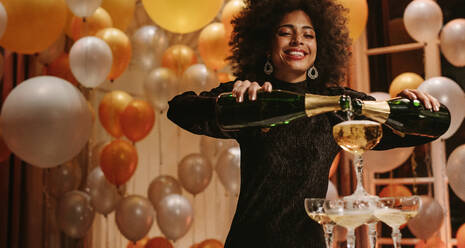 Afrikanische Frau gießt zwei Flaschen Champagner in Gläser Turm bei Gala-Nacht-Party. Frau füllt Pyramide von Gläsern mit Champagner. - JLPPF00077