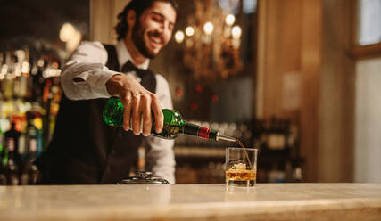 Barkeeper gießt Whiskey in ein Glas an der Theke. Barkeeper bereitet ein Getränk für einen Gast in einer Kneipe vor. - JLPPF00086