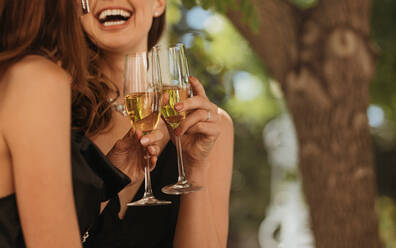 Close-up of two young women with drinks at a party. Female friends laughing while having champagne at a party. - JLPPF00095