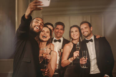 Hübscher junger Mann, der ein Selfie mit einer Gruppe von Freunden auf einer Neujahrsparty macht. Multi-ethnische Gruppe von Menschen, die sich auf einer Party vergnügen. - JLPPF00104