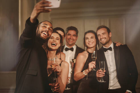 Handsome young guy taking selfie with group of friends at new years party. Multi-ethnic group of people enjoying at party. - JLPPF00104