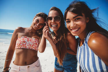 Porträt von drei jungen Freundinnen am Strand, die in die Kamera schauen und lächeln. Weibliche Freunde genießen den Sommerurlaub am Meer. - JLPPF00140