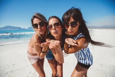 Porträt einer attraktiven jungen Frau mit Sonnenbrille, die sich am Strand Küsse zuwirft. Gruppe von Freundinnen im Sommerurlaub, die Spaß haben. - JLPPF00149