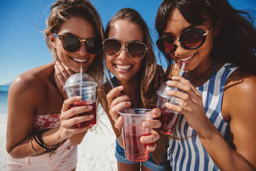 Close up Porträt von schönen jungen Frauen trinken kaltes Getränk am Strand. Lächelnde Freundinnen genießen Eistee am Meer. - JLPPF00161