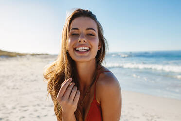 Porträt einer lächelnden jungen Frau am Strand an einem sonnigen Tag. Junges kaukasisches weibliches Modell im Bikini am Meeresstrand. - JLPPF00183