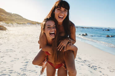 Porträt einer jungen Frau, die ihre Freundin am Strand huckepack nimmt. Mädchen genießen den Sommerurlaub am Meer. - JLPPF00194