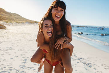 Portrait of young woman giving piggy back to her female friend on beach. Girls enjoying summer vacation at the sea shore. - JLPPF00194