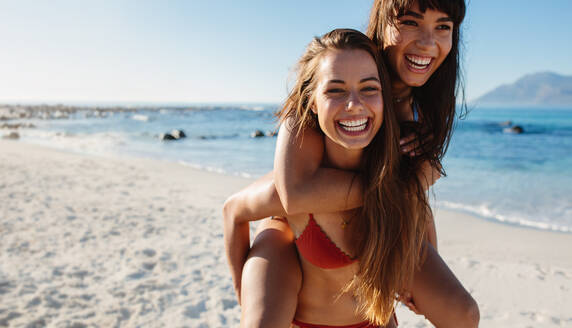 Porträt einer schönen jungen Frau, die ihre Freundin auf dem Rücken trägt. Junge Frauen, die den Sommerurlaub am Strand genießen. - JLPPF00196