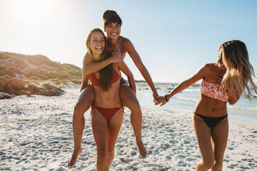 Eine Gruppe junger Frauen genießt eine Huckepackfahrt am Strand. Schöne Freundinnen haben Spaß am Strand. - JLPPF00204