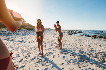 Smiling young women having fun on the beach. Female friends with water gun ready for fight. - JLPPF00217