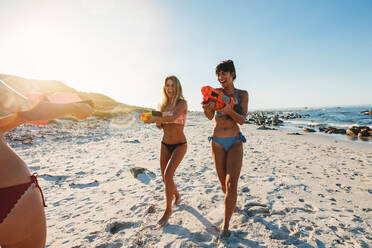 Junge Frauen amüsieren sich am Strand bei einer Wasserpistolenschlacht. Freundinnen genießen den Sommerurlaub am Meer. - JLPPF00218