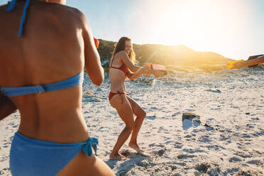 Freundinnen spielen mit Wasserpistolen am Strand. Zwei junge Frauen im Bikini liefern sich eine Wasserpistolenschlacht am Meer. - JLPPF00220