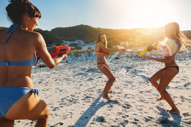 Junge Frauen amüsieren sich am Strand bei einer Wasserpistolenschlacht. Freundinnen genießen den Sommerurlaub am Meer. - JLPPF00221