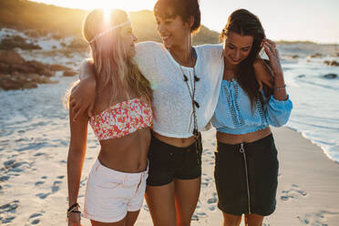 Happy young women strolling along coastline on a sunny day. Three female friends walking together on a beach, enjoying summer vacation. - JLPPF00230