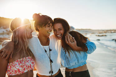 Porträt von drei jungen Freundinnen, die lachend am Meer spazieren gehen. Junge Frauen, die am Strand spazieren gehen. - JLPPF00231