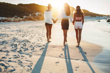 Rückansicht einer jungen Frau, die am Strand spazieren geht, in voller Länge von drei Freunden, die am Strand spazieren gehen und einen Sommertag genießen. - JLPPF00237