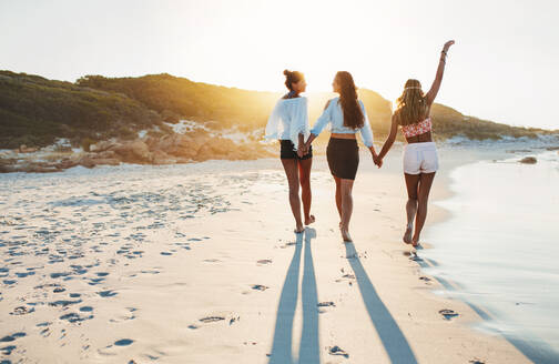 Rückansicht von jungen Frauen, die an einem Sommertag am Strand spazieren gehen. Männer und Frauen am Meer. Eine Gruppe von Freunden, die zusammen am Strand sind. - JLPPF00238