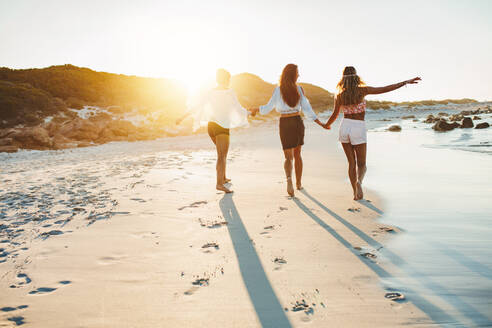 Rückansicht von drei jungen Freundinnen, die am Meer spazieren gehen. Junge Frauen, die am Strand spazieren gehen und sich amüsieren. - JLPPF00239