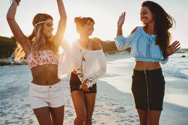 Aufnahme von stilvollen jungen Frauen, die sich an der Meeresküste vergnügen. Freundinnen, die an einem Sommertag am Strand tanzen und Spaß haben. - JLPPF00245