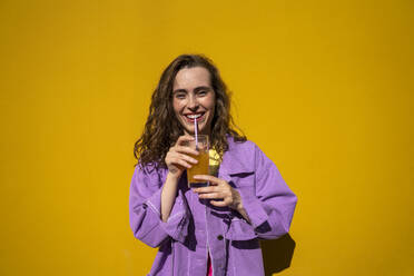 Happy woman drinking orange juice in front of wall - VPIF07327