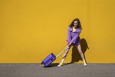 Woman pulling wheeled luggage in front of yellow wall - VPIF07339