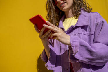 Frau in Jacke benutzt Smartphone in der Nähe einer gelben Wand - VPIF07344