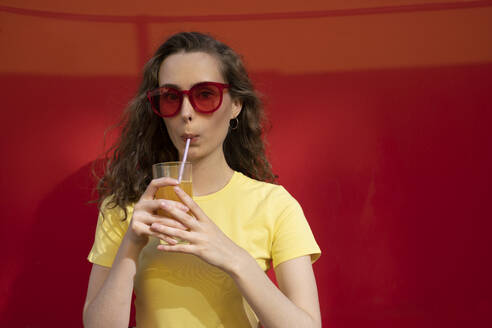 Frau trinkt Saft und trägt eine Sonnenbrille vor einer roten Wand - VPIF07358