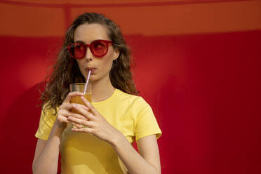 Contemplative woman drinking juice in front of red wall - VPIF07359