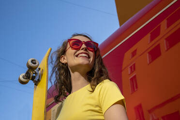 Glückliche Frau mit Sonnenbrille hält gelbes Skateboard - VPIF07363