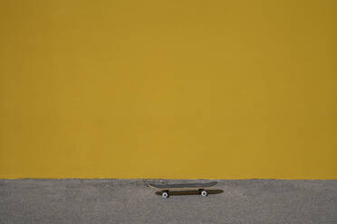 Skateboard on footpath in front of vibrant yellow wall - VPIF07365