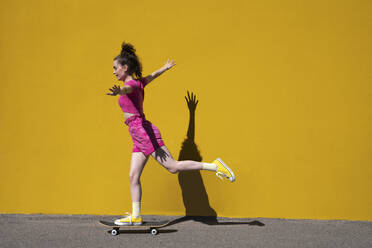 Frau mit ausgestreckten Armen balanciert auf einem Skateboard vor einer Wand - VPIF07366