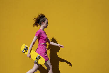 Young woman with skateboard walking in front of wall on sunny day - VPIF07370
