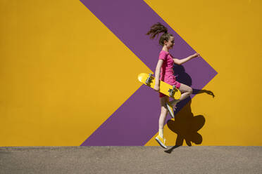 Woman with skateboard jumping in front of patterned wall - VPIF07371