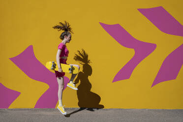 Woman with skateboard enjoying in front of patterned wall on sunny day - VPIF07372