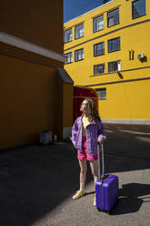Frau mit Gepäck auf Rädern steht in der Nähe eines Gebäudes an der Straße - VPIF07397